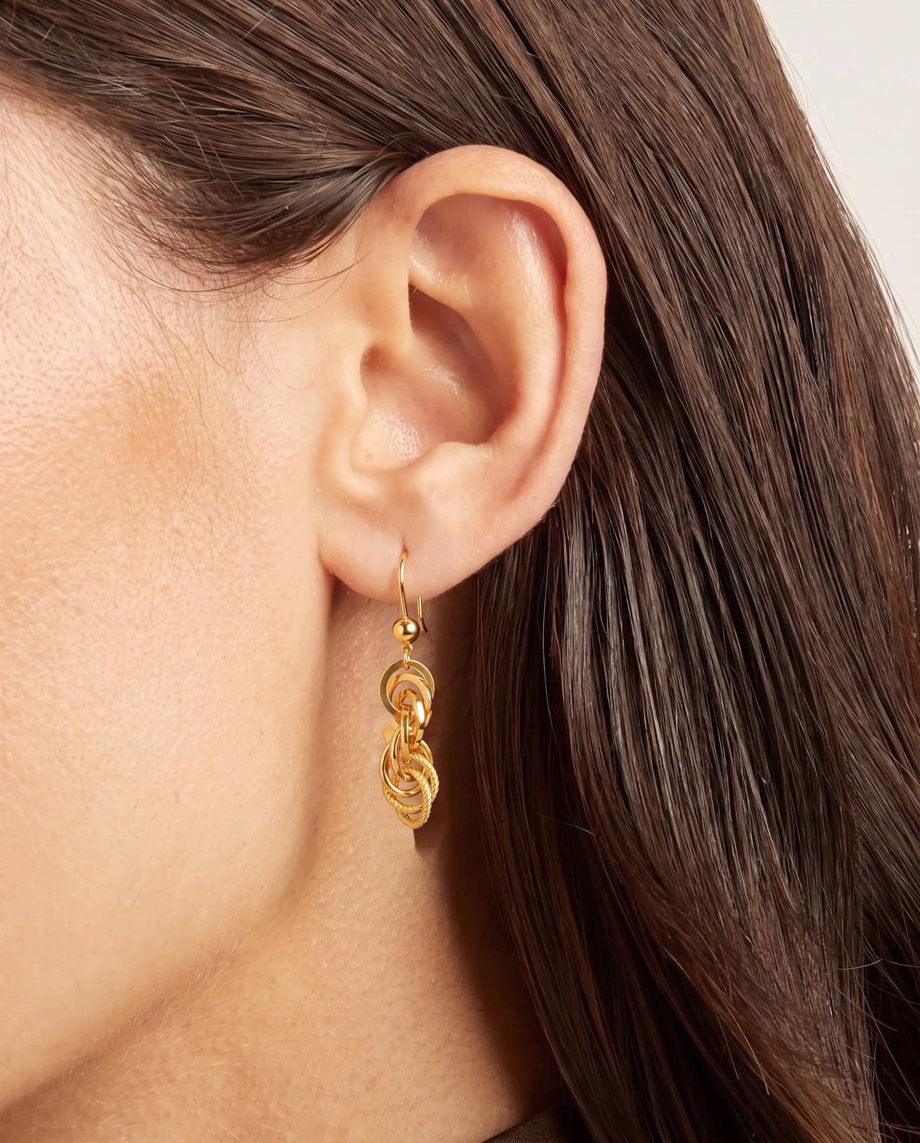 A model wearing the Polished and Rope Six-Oval Link Drop Earrings in 21K yellow gold